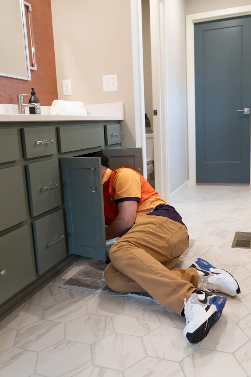 A Golden Plumbing technician at work beneath a bathroom vanity
